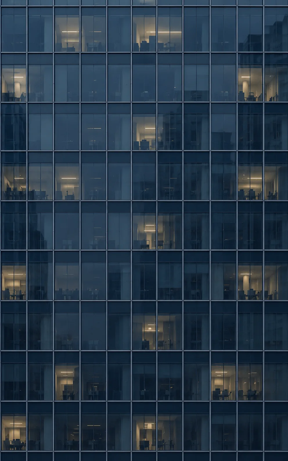 A curtain-wall façade at dusk, a sparse grid of lit windows